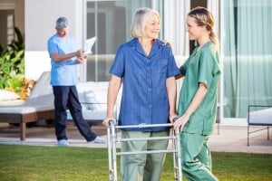 Friendly female nurse assisting senior woman to walk with Zimmer