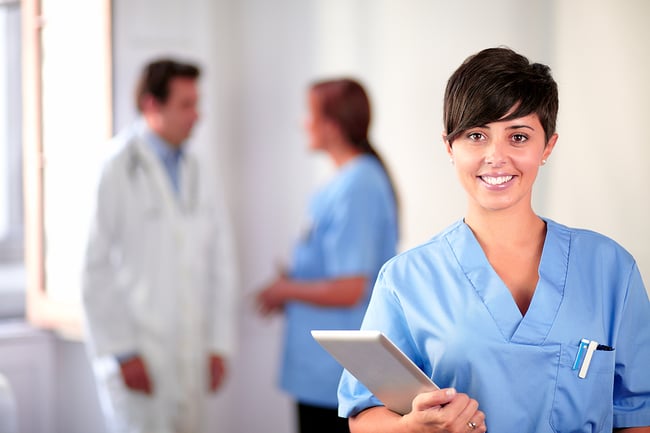 Medical assistant wearing blue scrubs and holding a clipboard