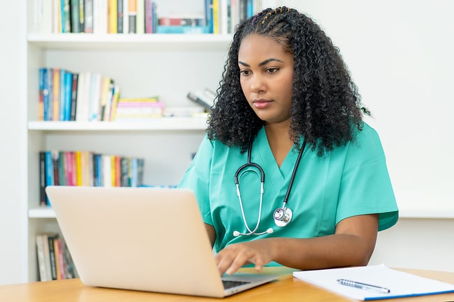 Female medical assistant sitting at a table in a doctors office focused on her work using a laptop