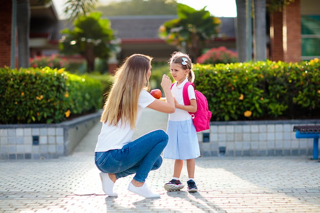 Preschool teacher helping a young student outside.