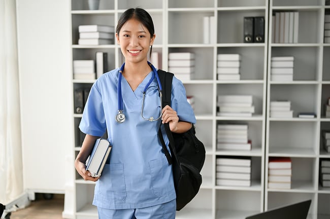 young woman wearing scrubs while holding backpack and books attending vocational school to become a medical assistant