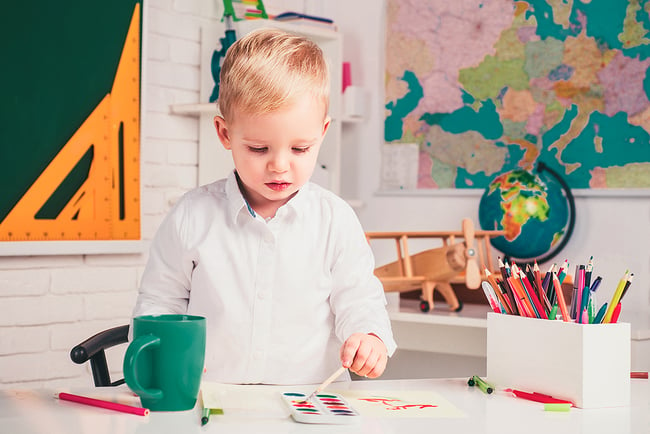 young boy using watercolor paints in a classroom
