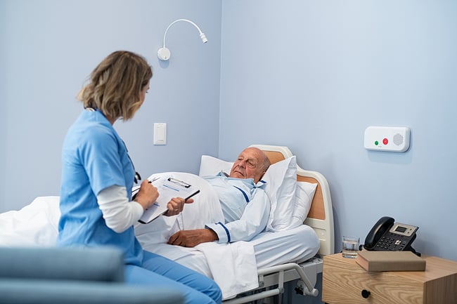 Medical assistant sitting at the bedside of a senior patient taking notes on a clip board