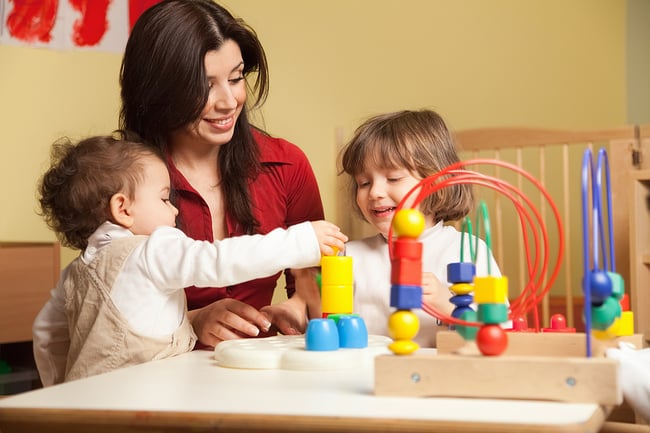 young female teacher sitting with two of her students playing with enrichment toys