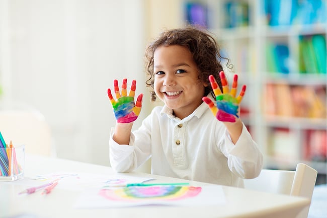 Preschool student finger painting in a colorful preschool classroom. 