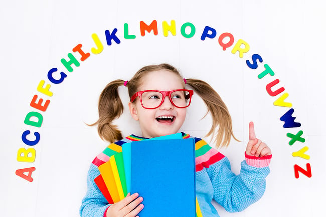 Preschool students wearing glasses holding colorful folders and pointing to the alphabet.