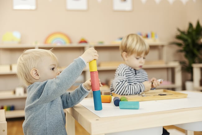 Young preschool students playing with wooden blocks at a classroom table.