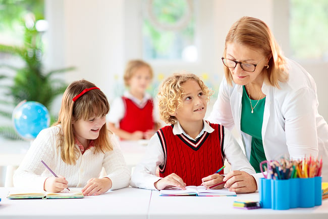 female preschool teacher standing by a couple of her students while they draw