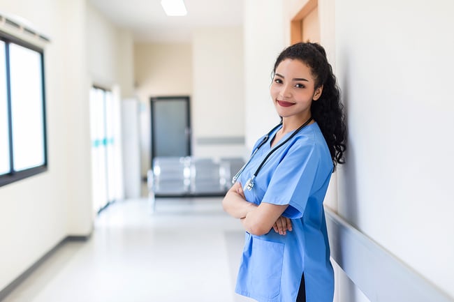 Medical assistant wearing blue scrubs standing in the hallway of a hospital.