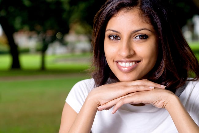 Female college student smiling with her chin on her folded hands.