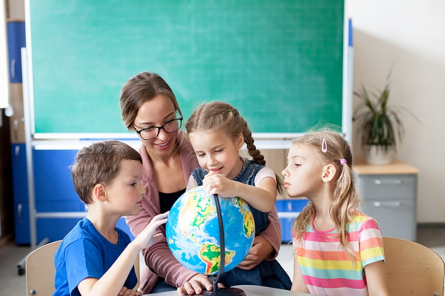 Young female teacher sitting with three of her students teaching them with a globe.