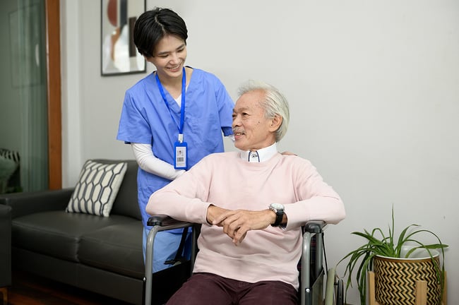 young medical assistant standing by an elderly man in a wheelchair smiling