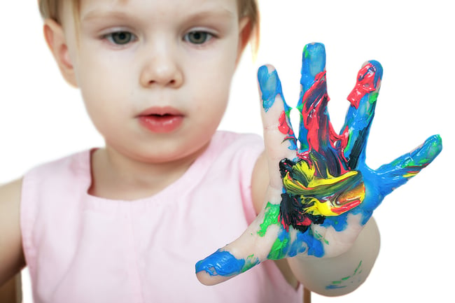 Very small child holding her hand up while fingerpainting. Young child has colorful paint all over her open hand.