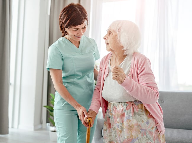 Smiling female medical assistant in an assisted living facility helping an elderly woman resident.