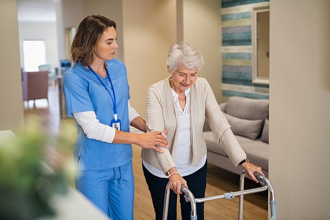 Medical assistant helping an elderly patient walk with a walker.