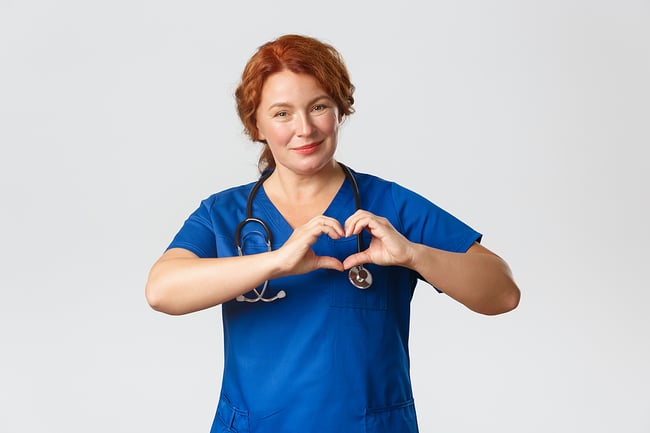 New medical assistant in scrubs smiling with her hands in a heart shape at her chest.