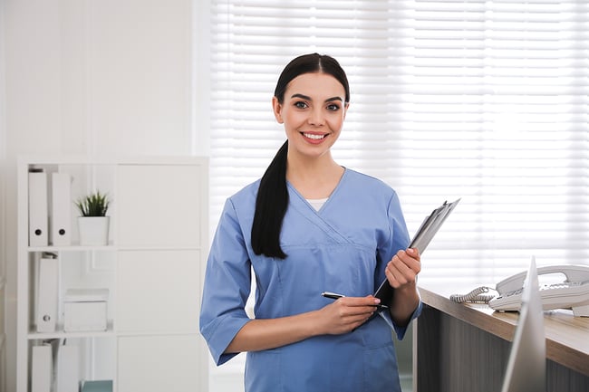Medical assistant working in a medical clinic holding a pen and clipboard.