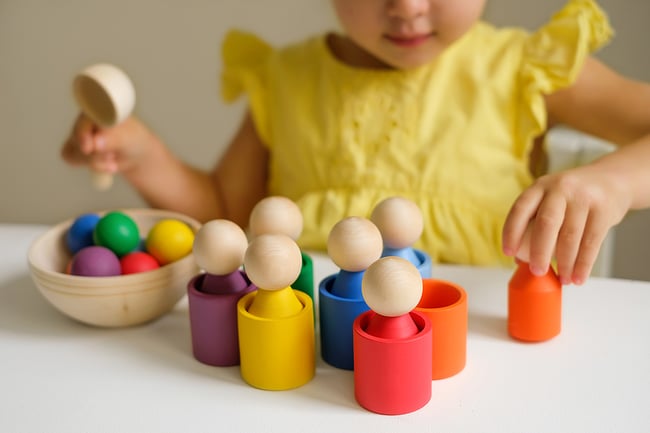 Preschool aged student playing with wooden toys painted in primary colors.