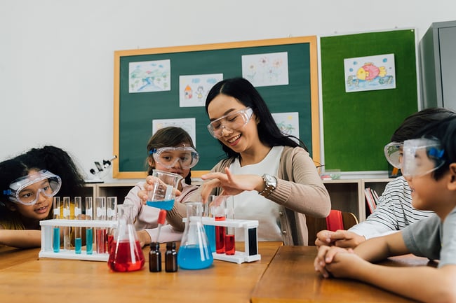 Smiling female teacher doing science experiments with a group of young students in a classroom. 